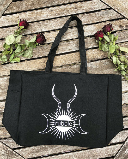 Rubble logo tote bag lays on wood surrounded by dried red roses.