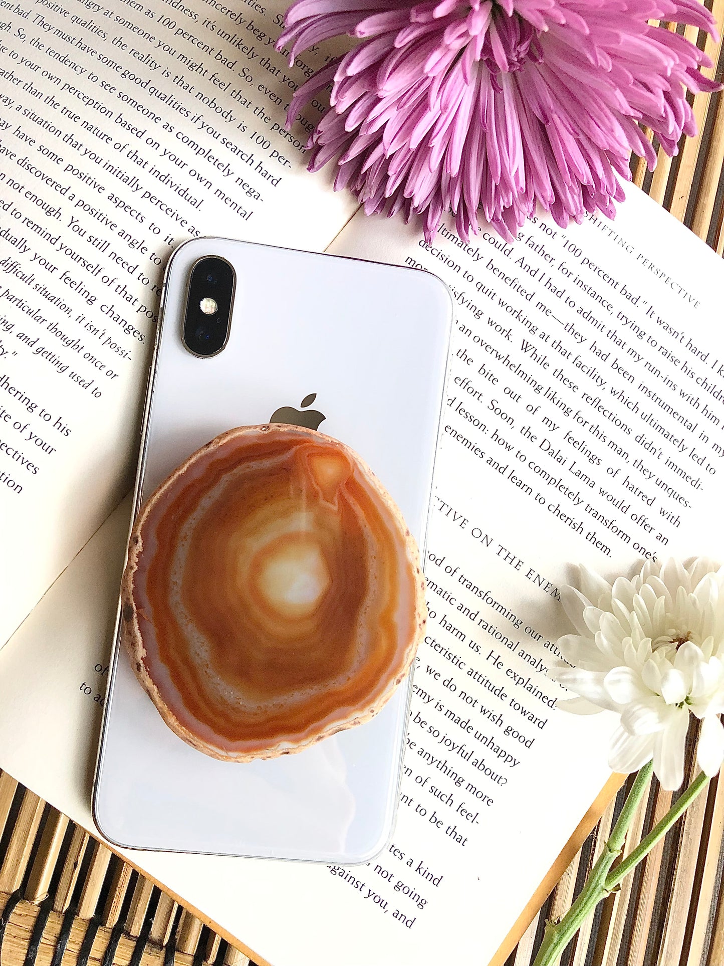 Natural agate phone grip presented on iPhone 8, laying on top of open book, framed by for and yellow flowers