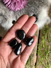 Load image into Gallery viewer, Hematite tumbled stones lay in hand over boho background of flowers and fur
