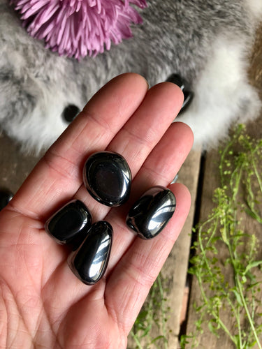 Hematite tumbled stones lay in hand over boho background of flowers and fur