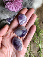 Load image into Gallery viewer, Purple Chevron Amethyst tumbled stones lay in hand over boho background of fur, foliage and aged wood.
