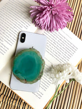 Load image into Gallery viewer, Natural greenish blue agate phone grip presented on iPhone 8, laying on top of open book, framed by for and yellow flowers
