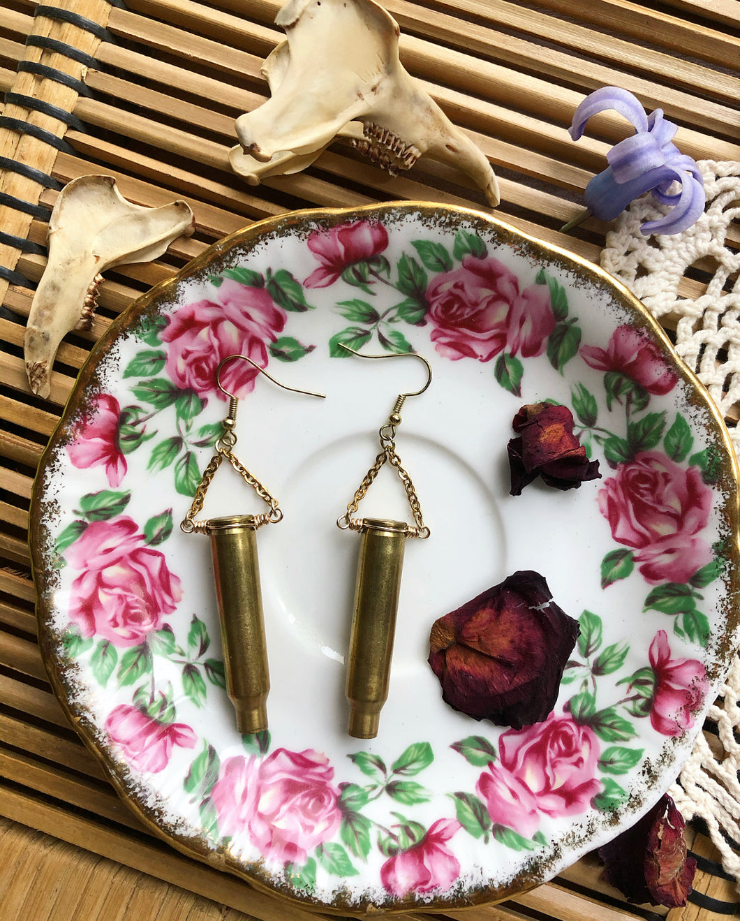 Golden brass bullet shell earrings lay on floral print plate with rose pedals and lace.