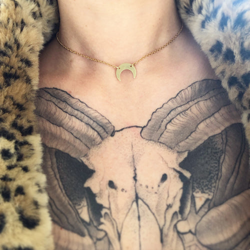 Golden crescent moon choker worn on neck with tattooed chest and leopard fur coat. 