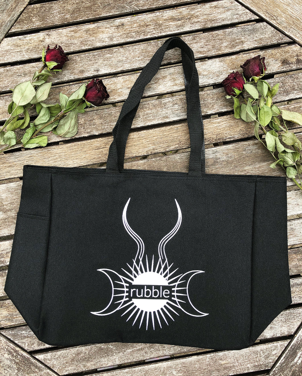 Rubble logo tote bag lays on wood surrounded by dried red roses.