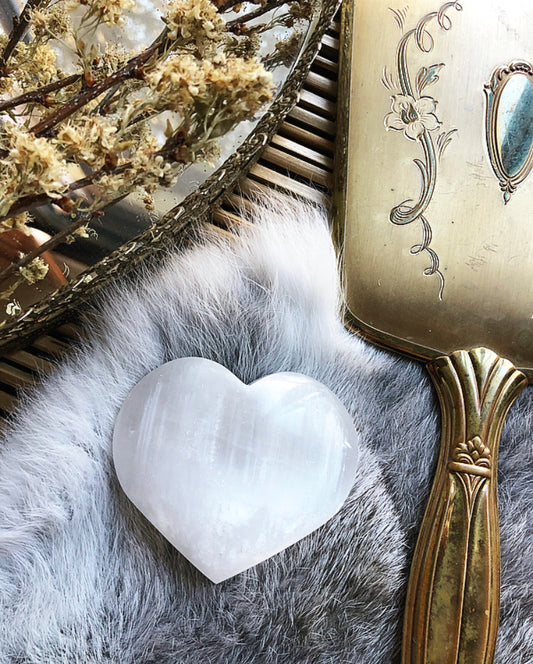 Large white Selenite palm stone lays on grey fur, next to golden brass mirror tray and matching vintage hand mirror.